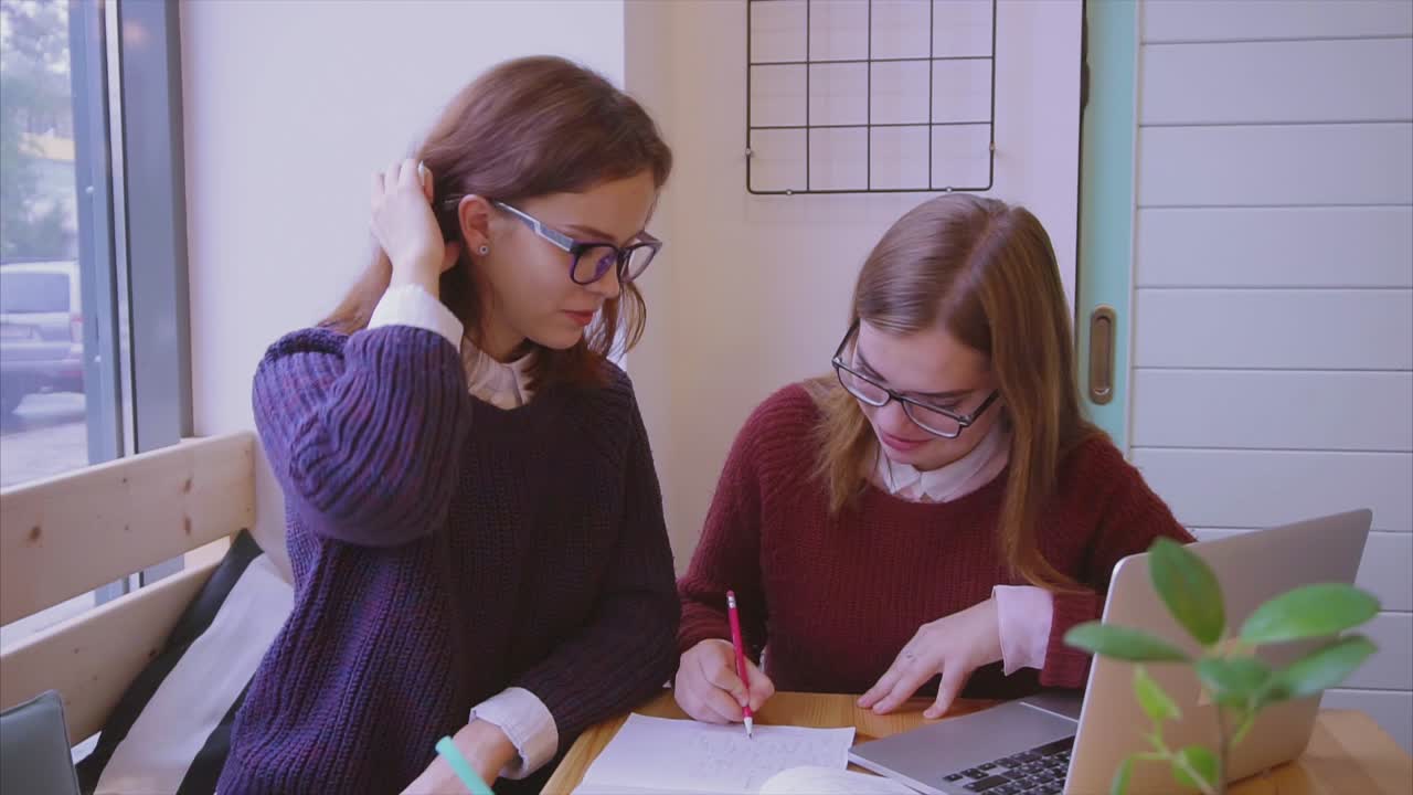 dos mujeres jóvenes estudiando juntas en un café