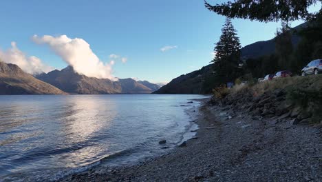 tranquil lake surrounded by mountains under clear skies, captured in queenstown, new zealand. soft lighting enhances the peaceful atmosphere