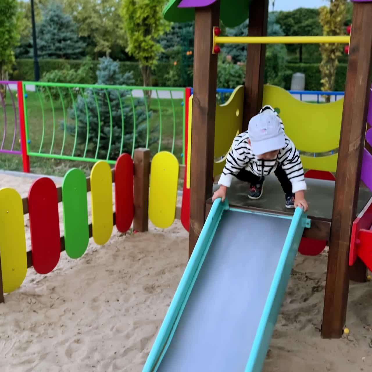 かわいい男の赤ちゃんが、遊園地で楽しそうに遊んでいます。活発な子供は金属製の滑り台で足を打ちつけ、幸せそうに微笑んでいます。