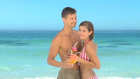happy couple posing drinking cocktails in front of the sea