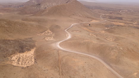 a lone vehicle travelling on long and winding desert road at fuerteventura, canary islands, spain