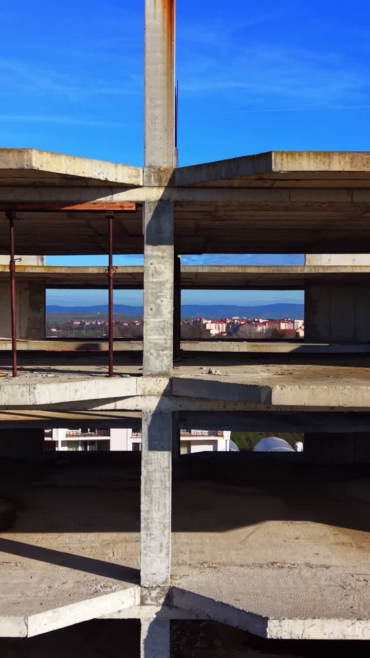 Struttura aperta di un cantiere incompiuto. Vista aerea di una città attraverso lo scheletro di un edificio in cemento. Video verticale