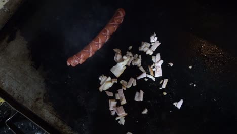 hand-held shot of sausage and onions being cooked on a grill in a restaurant