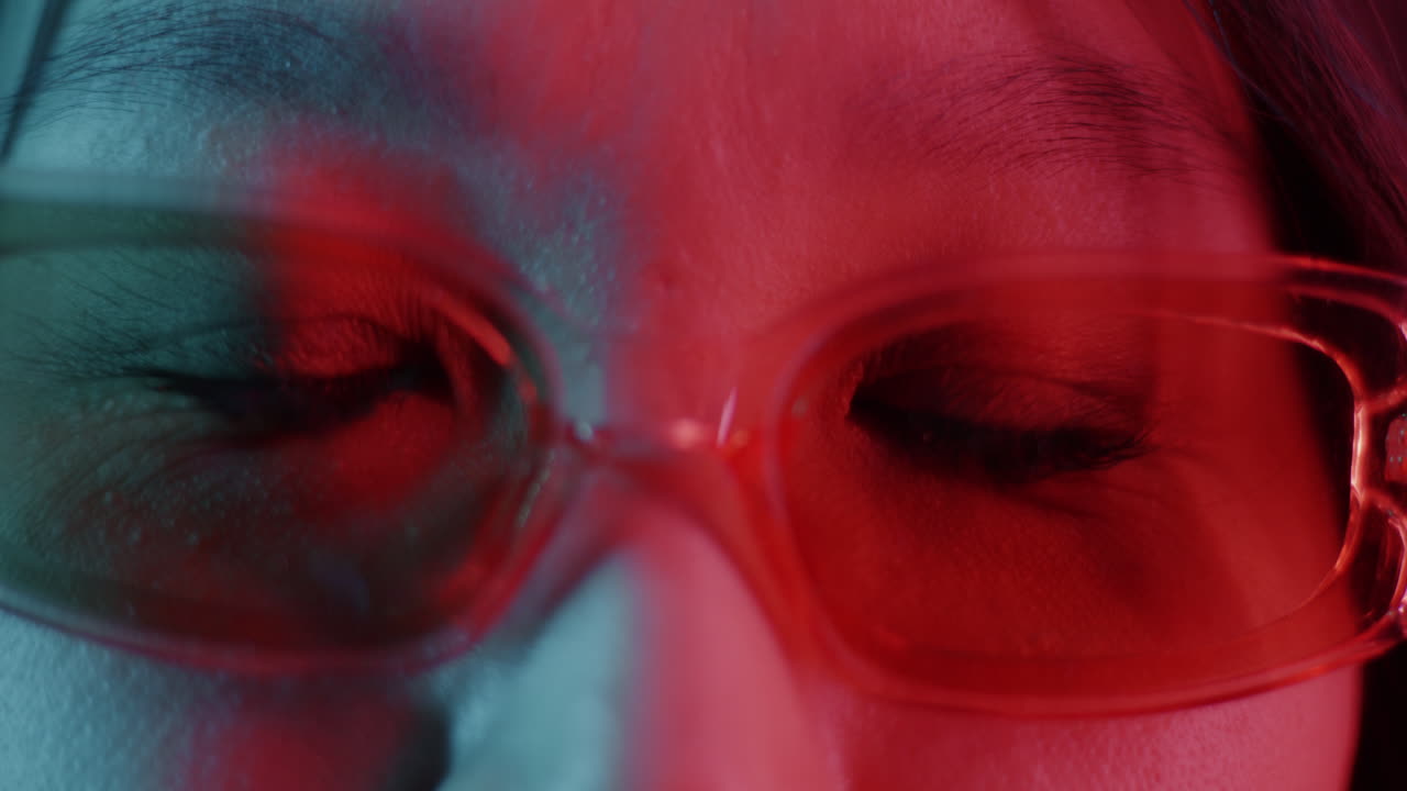 Close-up of a woman wearing glasses with vibrant colored lighting.