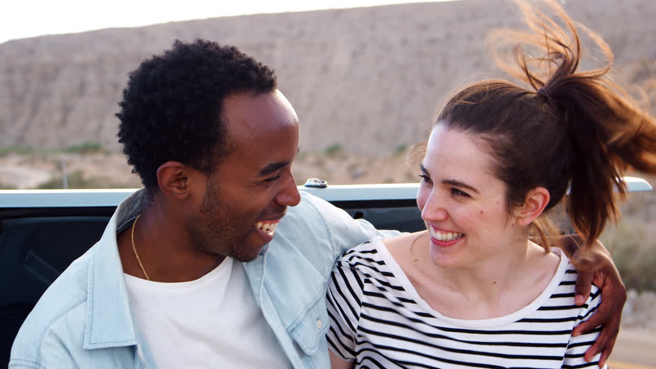 Happy mixed race couple sitting on car at roadside, close up