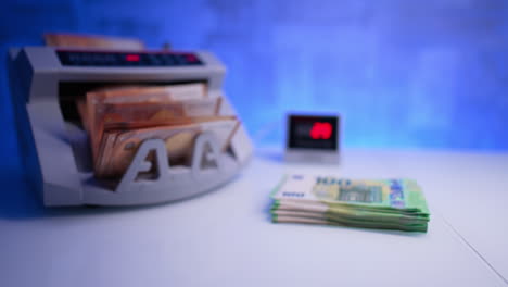 starting cash counting machine. fifty euro banknotes are processed in the equipment. one hundred euro stack lies on the desk. blurred image.