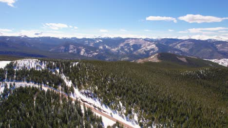 aerial drone establishing shot flying over snowy alpine forest hills with rocky mountains range in the background near mount evans colorado usa