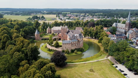 Kasteel-Huis-Bergh:-Luftaufnahme-Im-Orbit-Des-Fantastischen-Schlosses-Und-Betrachtung-Des-Wassergrabens,-Der-Nahegelegenen-Bäume,-Der-Türme-Und-Der-Nahegelegenen-Kirche