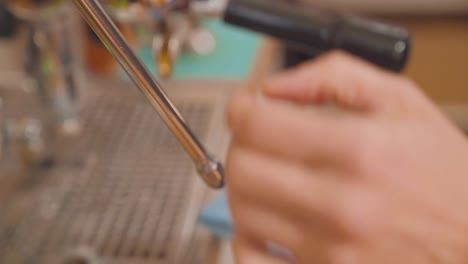 barista cleans steam wand of coffee machine with cloth and steam