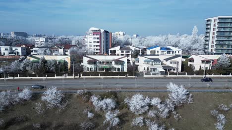 Vehículos-Circulando-Por-La-Carretera-Pasando-Por-Edificios-Y-árboles-Cubiertos-De-Hielo-En-Invierno-En-Galati,-Rumania