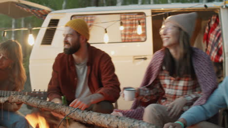 happy friends singing to guitar at campsite