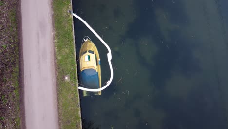 Ascend-aerial-top-down-of-sunken-old-speedboat-docking-on-river-shore-of-port