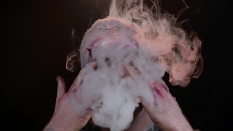 Sinister-man-with-horrible-scary-Halloween-zombie-makeup-in-costume-blows-smoke-from-nose-and-mouth