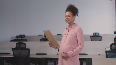 portrait of a beautiful pregnant woman holding documents and smiling at camera while working in the office