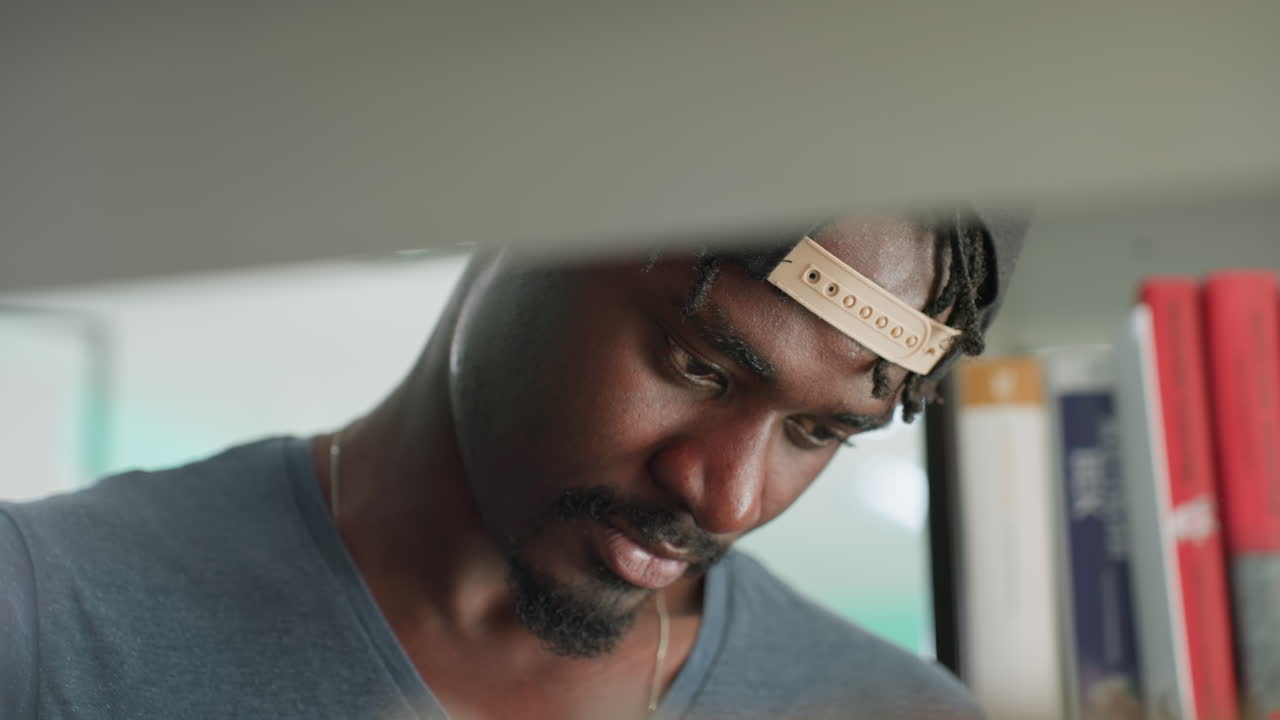 Close up of man seen through shelf in library, head tilted, intent gaze scanning books, shallow depth, soft bokeh, quiet study mood, focused search for next title, moment between stacks
