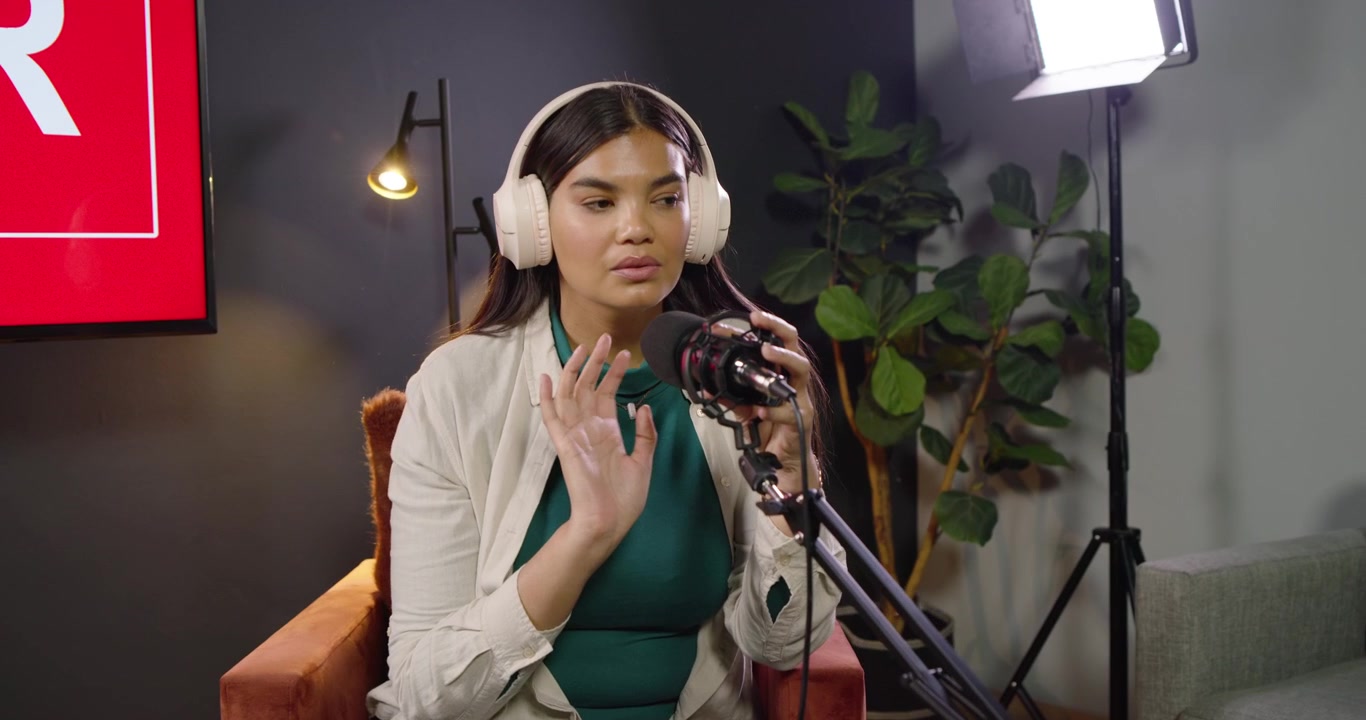 Afroamerikansk kvinde justerer/tager headset af, tjekker noter og telefon, mens mikrofonen er tændt i studiet.