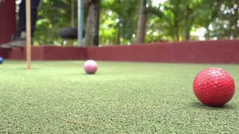 Tiro-Cercano-Y-Bajo-De-Una-Pelota-De-Golf-Que-Entra-En-El-Hoyo-En-El-Green-Del-Campo-De-Minigolf