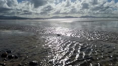 Hazy-Snowdonia-mountain-range-across-idyllic-slow-motion-shimmering-Irish-Seascape-from-Newborough-beach-shoreline