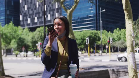 Mujer-Afroamericana-Con-Máscara-Hablando-En-Un-Teléfono-Inteligente-Sosteniendo-Café-En-La-Calle