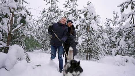 people on a walk in the forest. a man and a siberian husky dog are pulling a sleigh with a child in the snow in the forest. a woman is walking in the forest