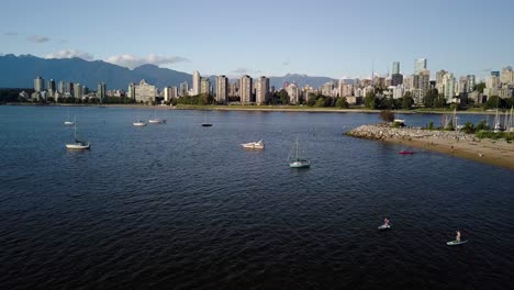 famous kitsilano beach with sailboats and people kayaking on the ocean