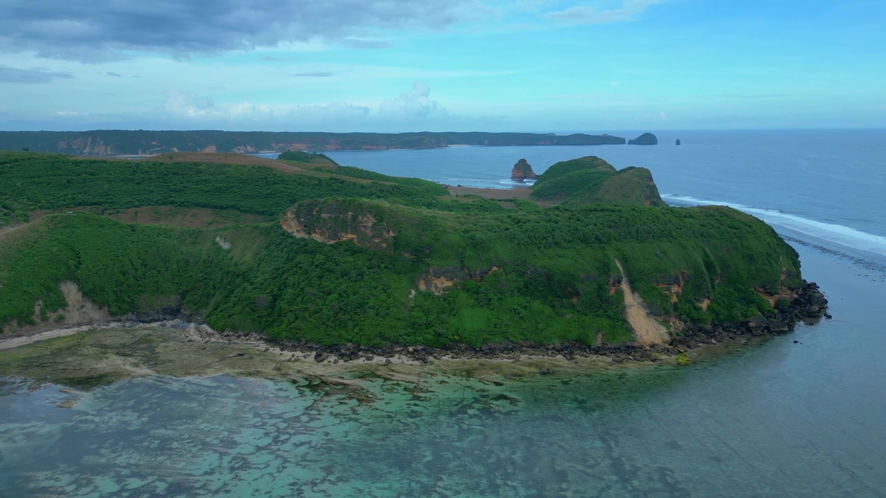 Vista da costa da ilha de Lombok mostrando colinas verdes encontrando o oceano azul claro com recifes de coral rasos e ondas suaves. Ótima vista aérea panorâmica de drone de cima.