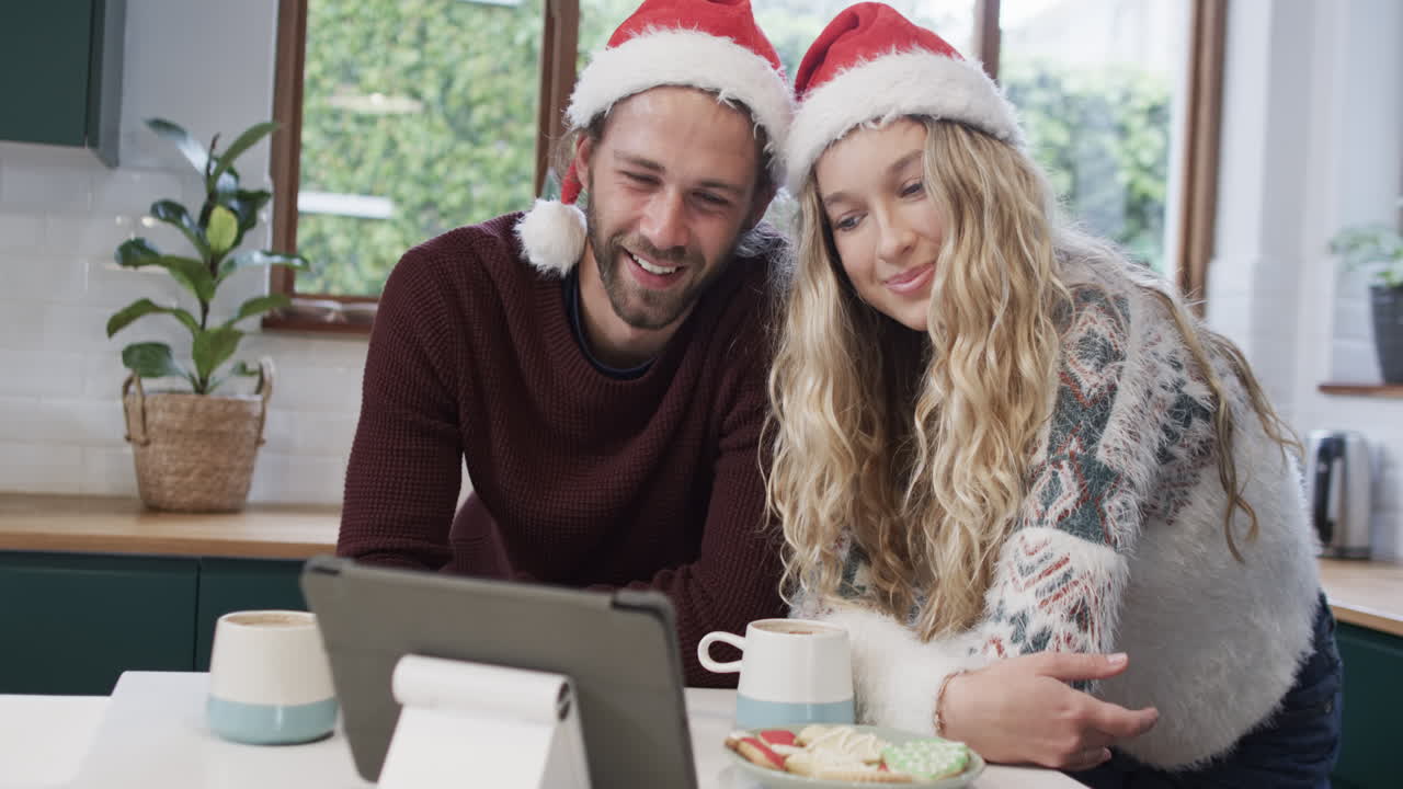 una pareja diversa con sombreros de santa usando una tableta para una llamada de video de navidad, en cámara lenta