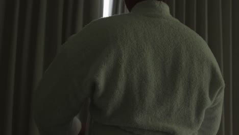 happy african american woman wearing robe, opening curtains and looking through window