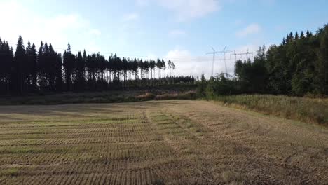 Drone-shot-flying-over-a-harvested-farm-field-surrounded-by-forest-in-sun