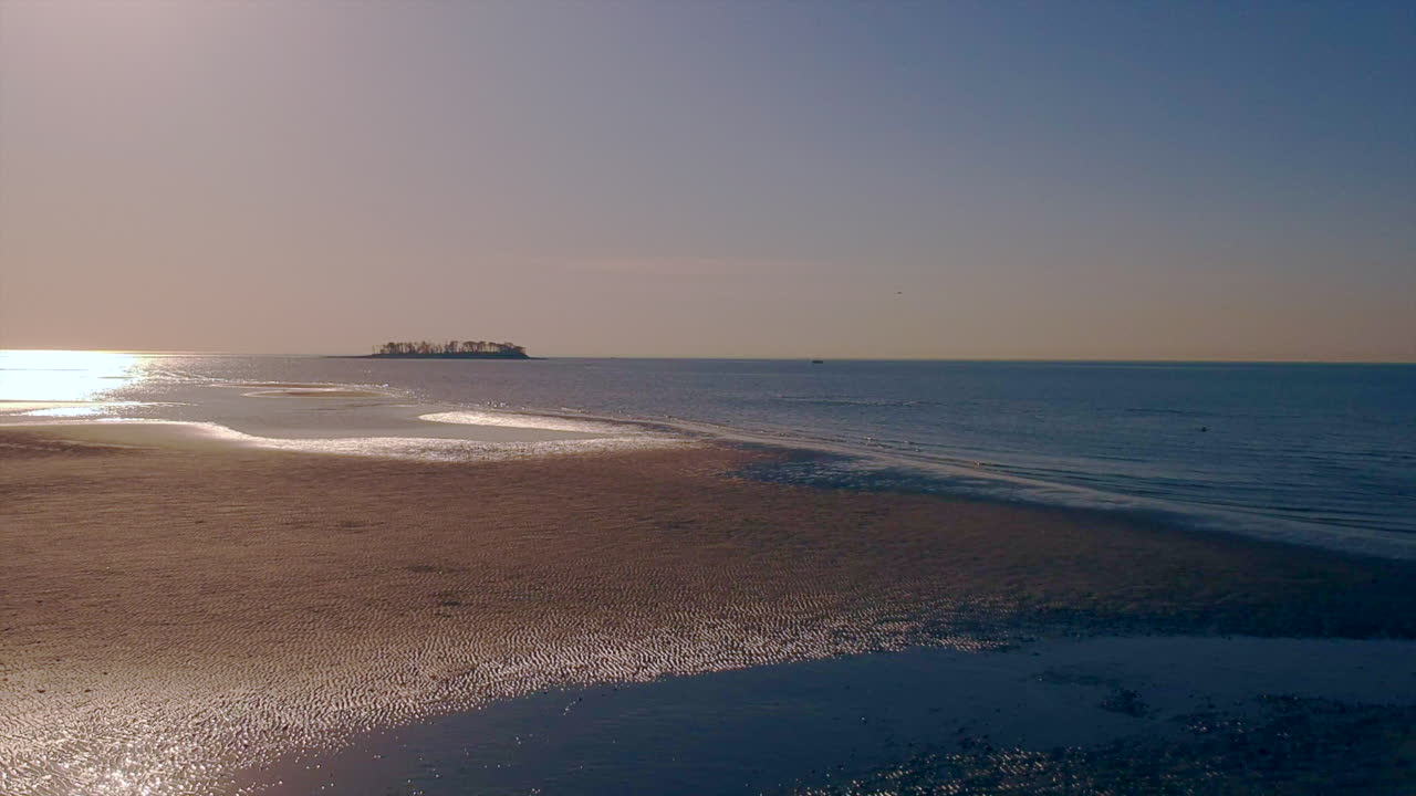 Drone panning back on a beach with an island in the distance