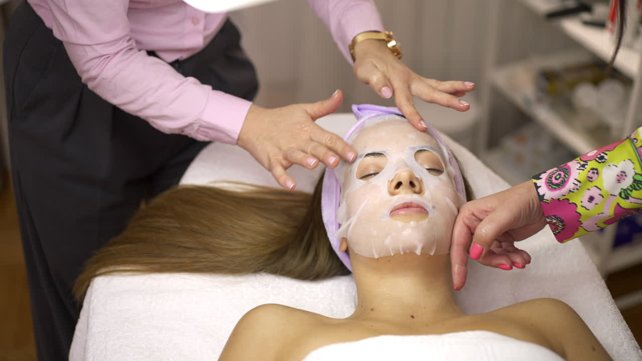 Woman receiving a facial sheet mask treatment from a cosmetologist