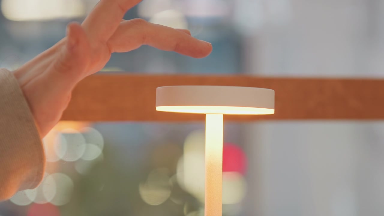 Nærbilde av en hvit sylindrisk gjenstand utstilt med myk belysning og bokeh-bakgrunn. En hånd nærmer seg toppflaten uten å berøre den, og opprettholder avstand gjennom hele scenen.