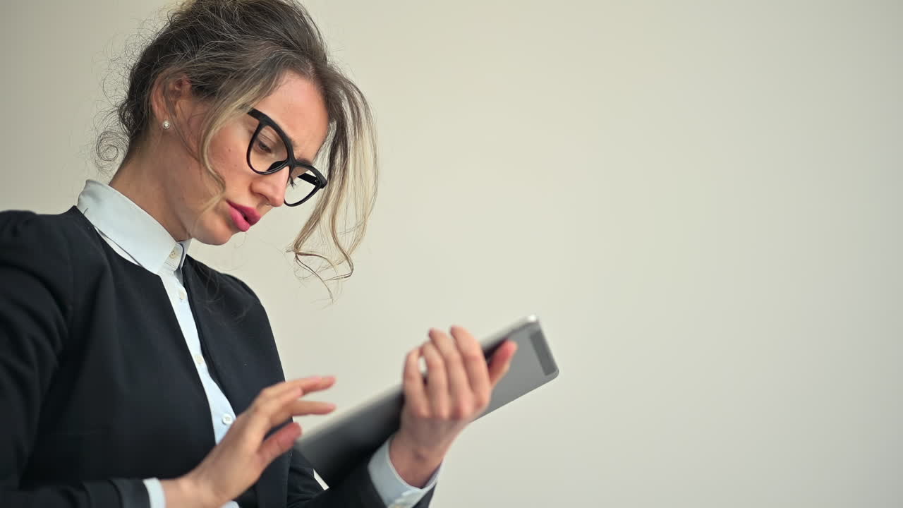 A businesswoman holding a digital tablet while looking thoughtful and stressed