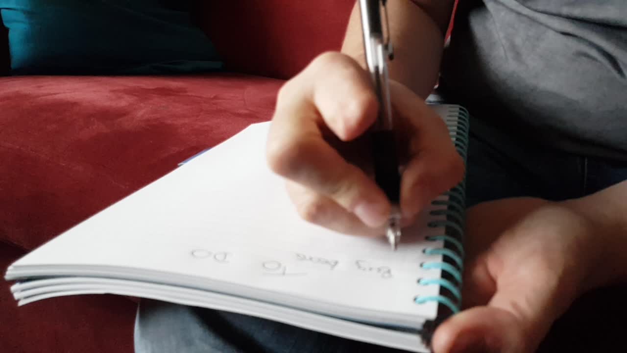 Male with a partially amputated index finger on his right hand sat down holding a pen and pad  writing a to do list.