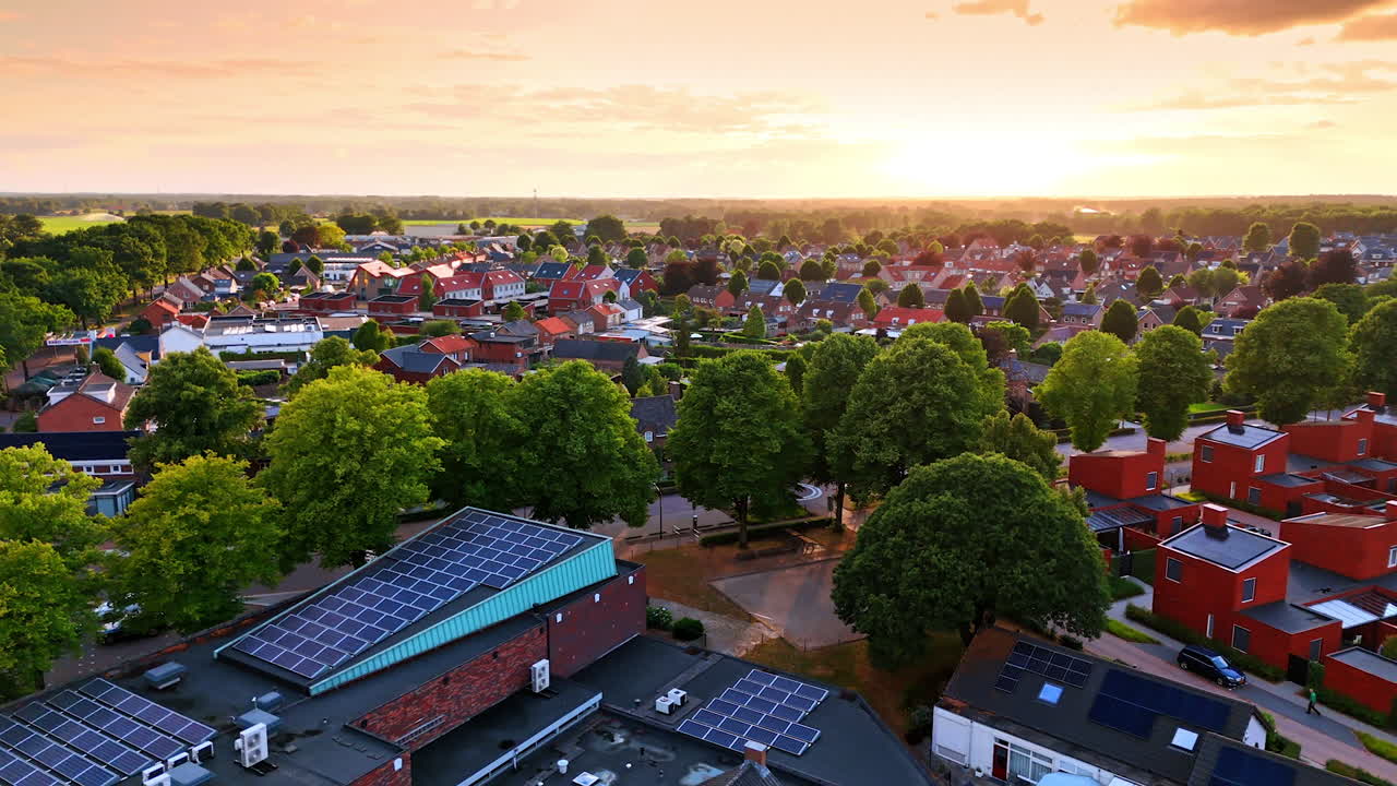 Idyllic view of the lovely town at sunset surrounded by lush greenery. Drone flight approaching a building with solar panels on top