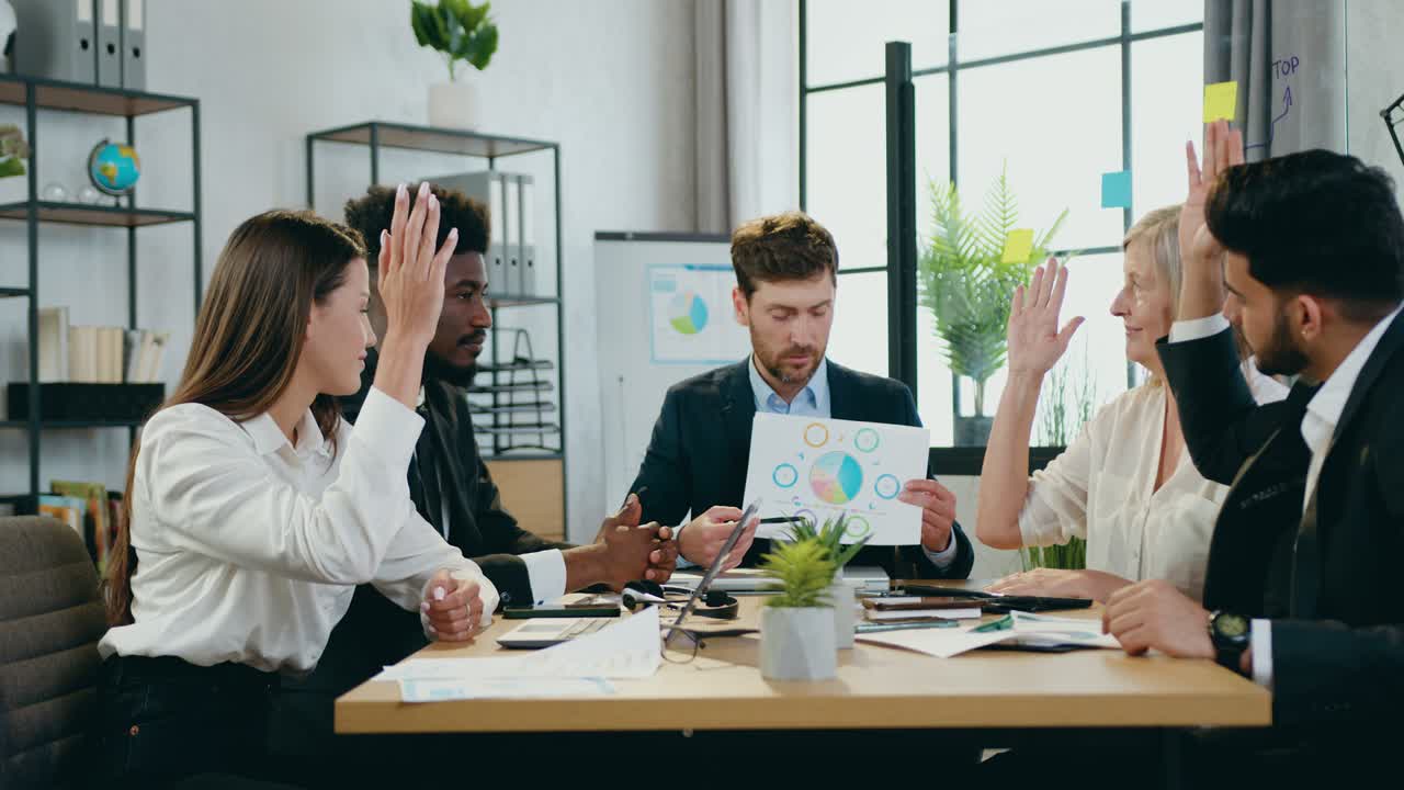 매력적이고 성공적이며 동기부여가 다양한 연령대의 다인종 사업가들이 이사회 테이블에 앉아서 주요 매니저의 방에서 비즈니스 컨퍼런스에서 손을 들어서 투표하고 있습니다.