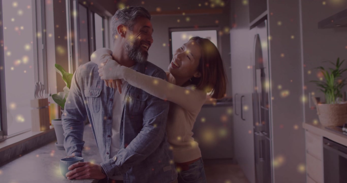 Couple sharing warm hug at counter with man holding mug laughing amid sparkles in lifestyle kitchen