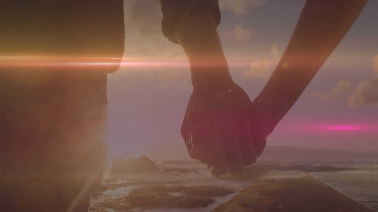 太陽が海に沈み、レンズフレアが手をつなぐカップルの上に広がり、映画の中で一体感を示している。