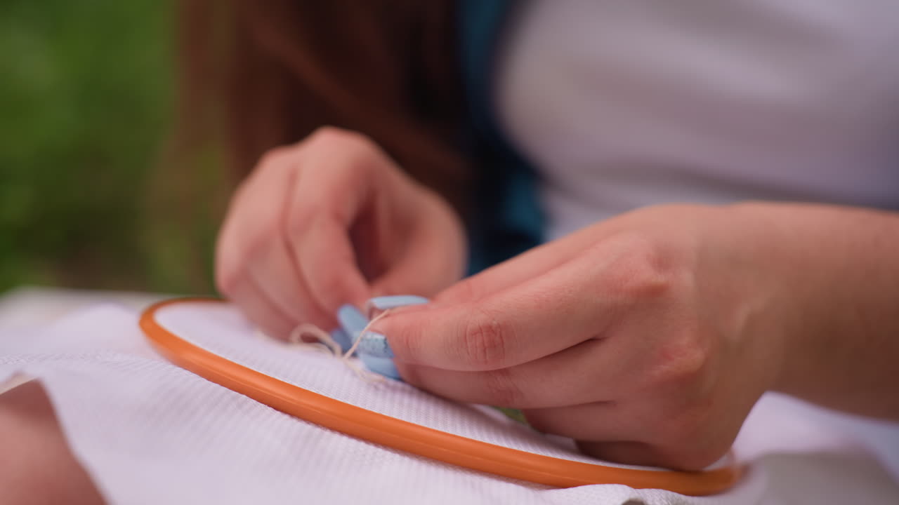 Close up of female hands carefully embroidering fabric with needle and thread in soft daylight, gentle motion showing focus, precision, and patience