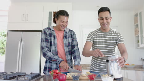 una feliz pareja gay diversa preparando un batido de frutas saludable en la cocina, espacio de copia, cámara lenta