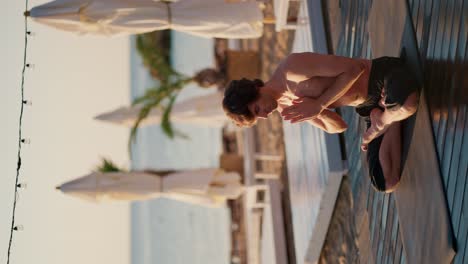 un tipo con pantalones cortos negros se sienta en una alfombra y hace yoga en la playa por la mañana. clases de meditación para calmar la mente. armonía del cuerpo y la mente