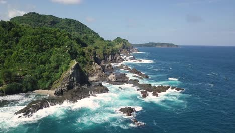 Drone-shot-of-overgrown-mountain-with-cliffs-and-giant-rocks-at-coastline-of-Siung-Beach-during-sunlight---Panorama-view