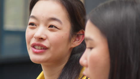 close up of two young female friends sitting on steps eating hot dogs bought at street food market stall 1