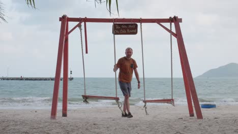 White-Man-stands-up-from-A-Swing-after-Enjoying-The-View-Of-The-sea-From-Sandy-Shore-In-Con-Dao,-Vietnam