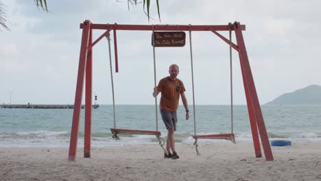 white man stands up from a swing after enjoying the view of the sea from sandy shore in con dao, vietnam