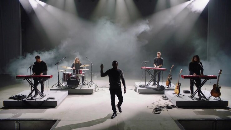 Cantante in abiti scuri che entra in scena a tempo, muovendosi verso la telecamera in studio, con le chiavi, coinvolgendo il pubblico.
