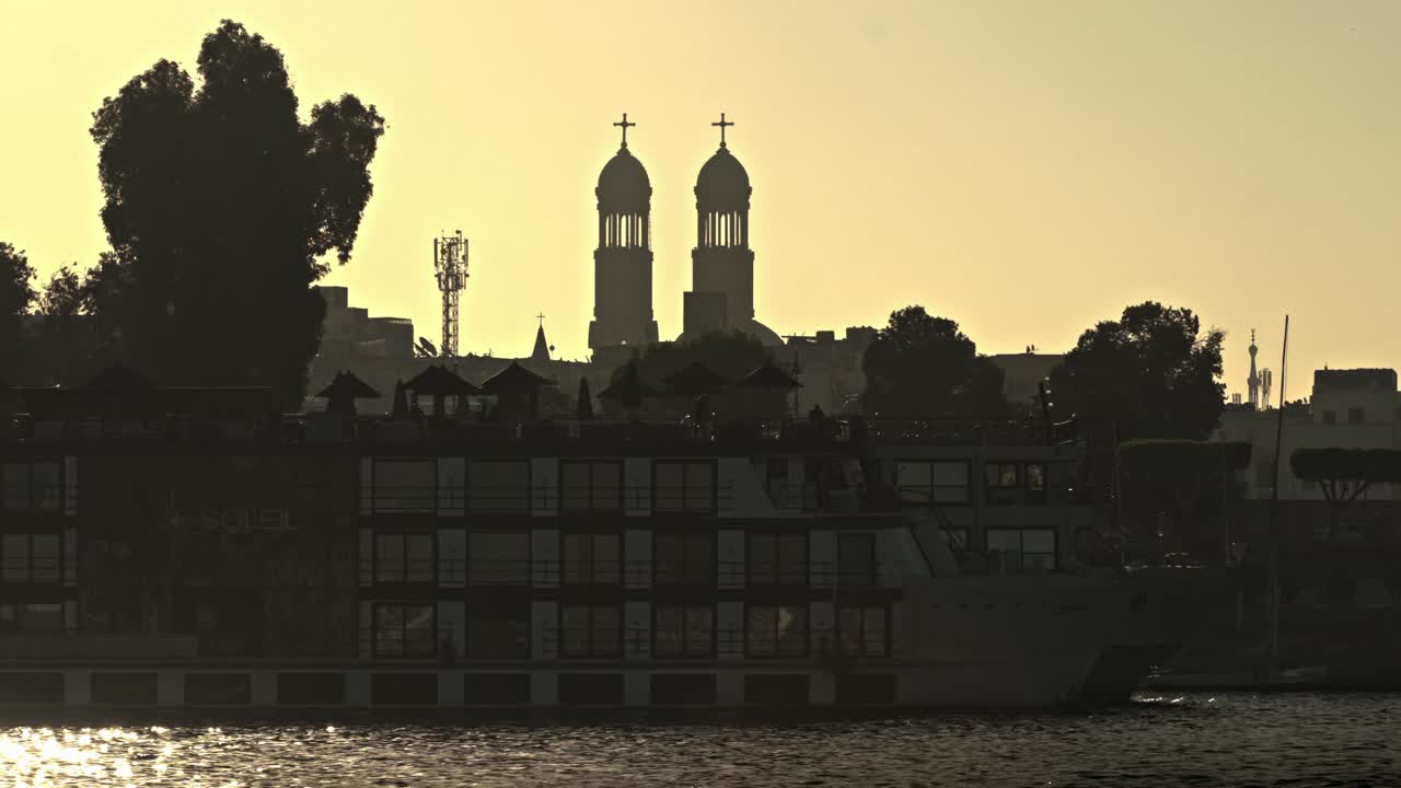 Situata in posizione prominente sulla sponda orientale del Nilo a Luxor, Egitto, questa silhouette cattura l'architettura svettante della Cattedrale Copta Ortodossa di San Michele Arcangelo.