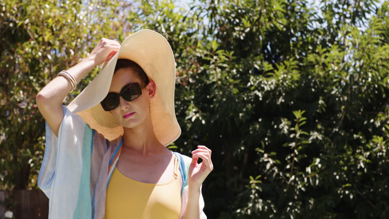 Woman in sunglasses enjoying sunny day by pool, holding towel confidently