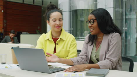 diverse businesswomen using laptop and speaking at work