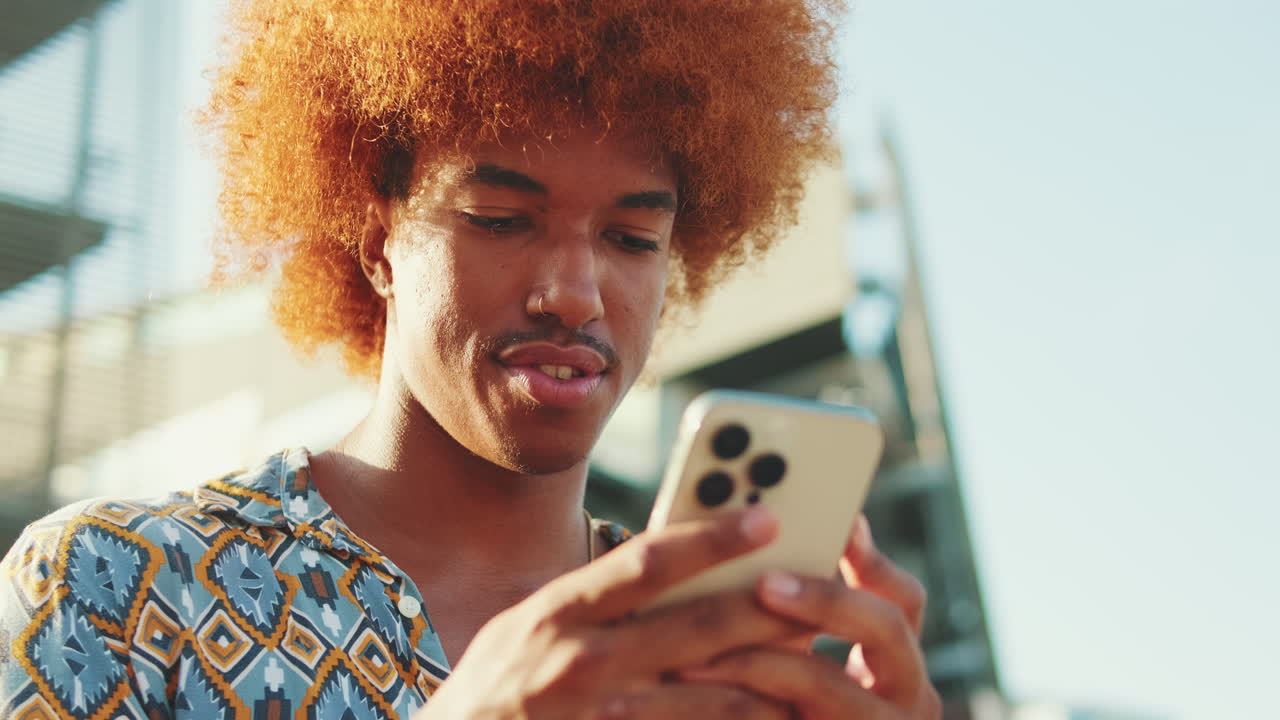 Uomo con taglio afro che usa lo smartphone all'aperto